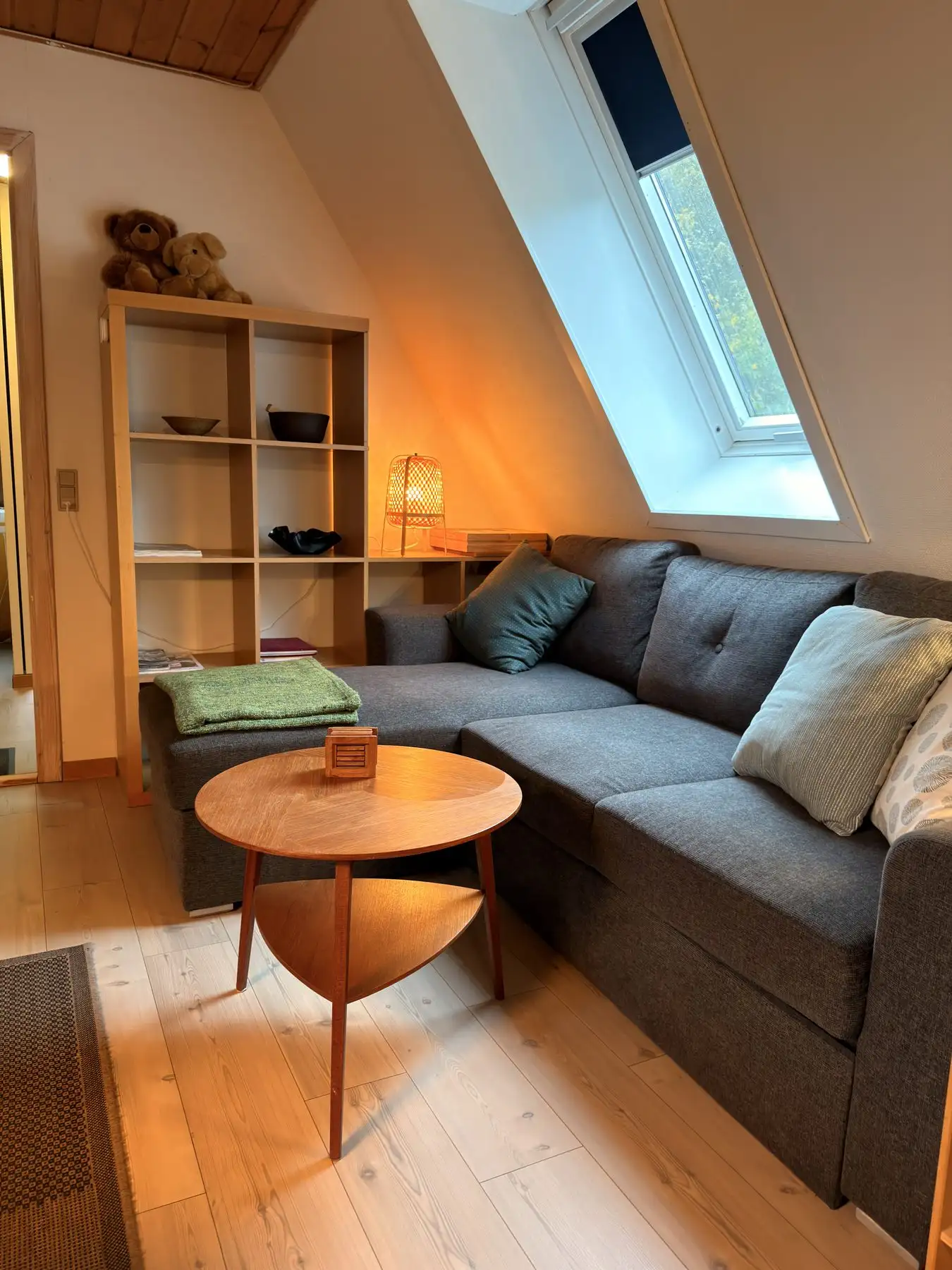 Stuen i lejligheden med hjørnesofa, sofabord og reol under ovenlysvinduet